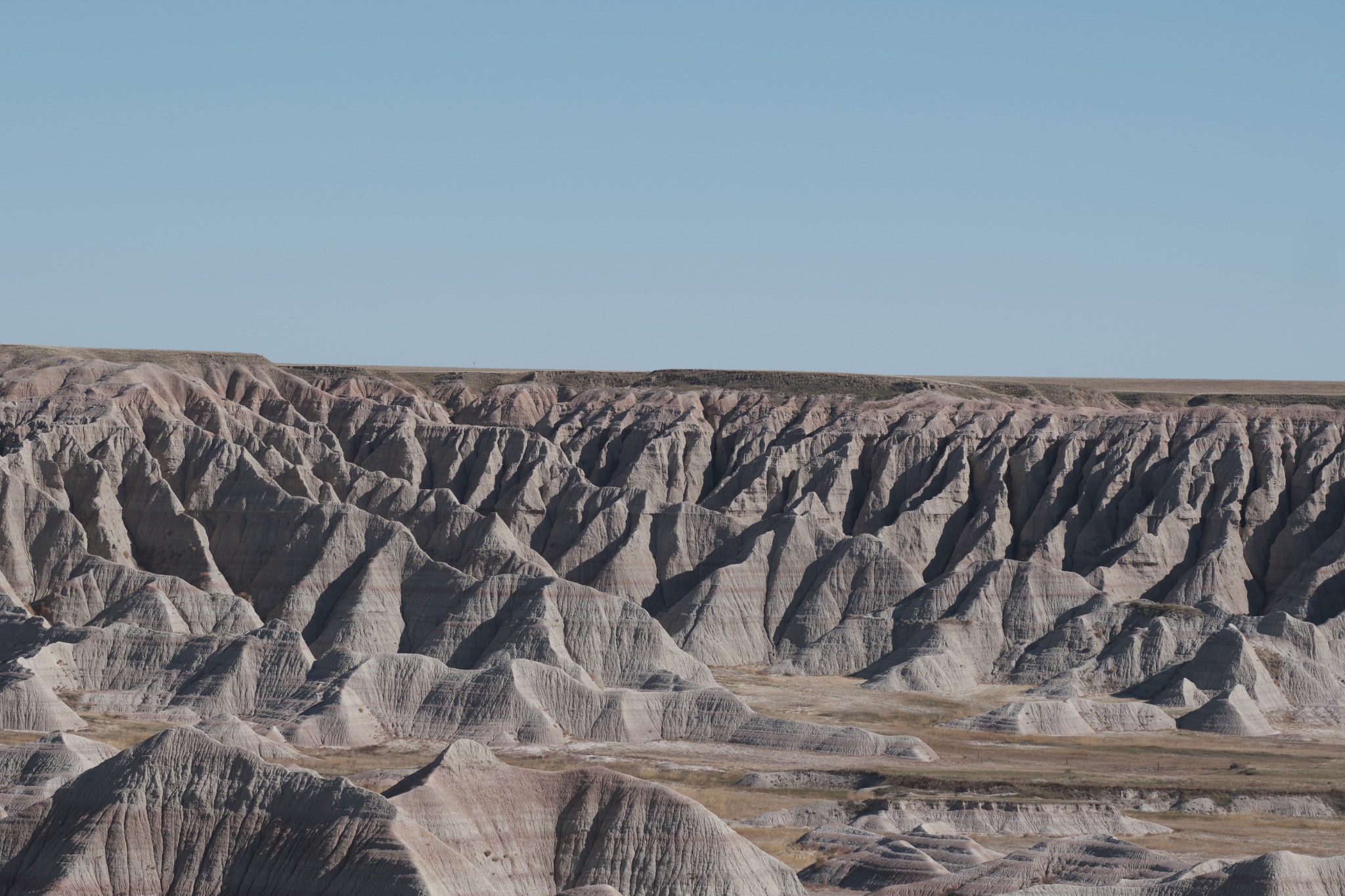 Quiet rock formations beneath an open blue sky in Badlands, South Dakota