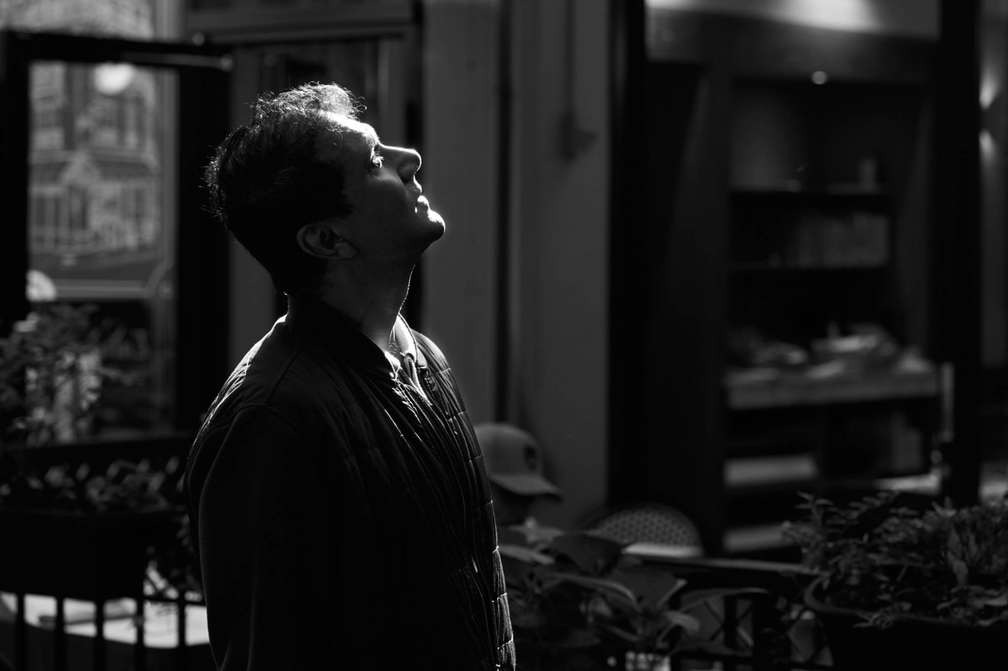 A man in profile looking upward into a shaft of light, photographed in black and white