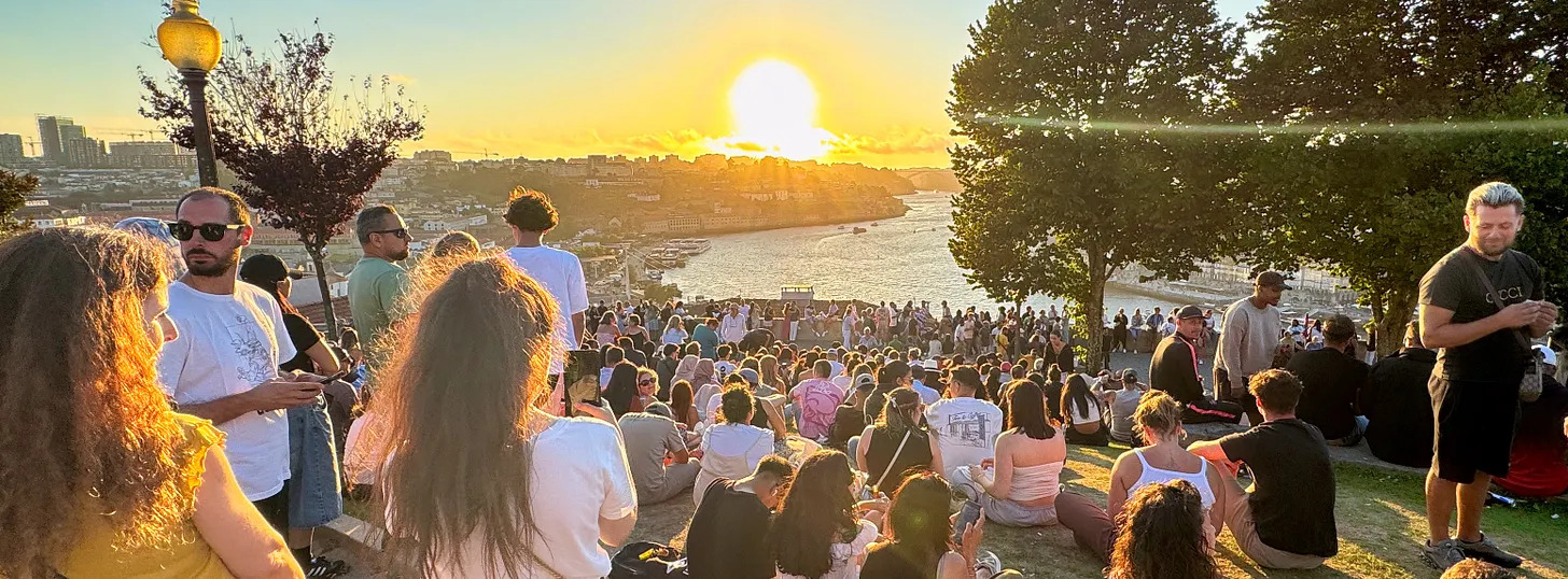 A crowd gathered at Jardim do Morro in Porto as the sun sets over the Douro River